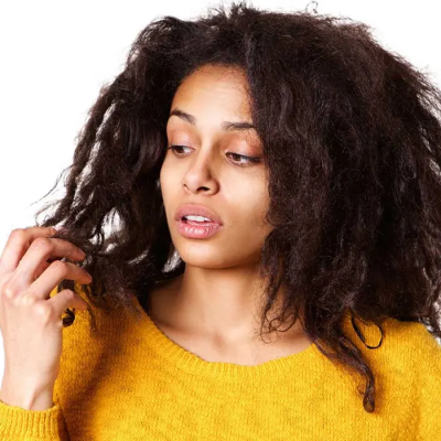 Get the Facts About Chemical Relaxers and Hair Loss - a woman in a yellow sweater inspecting her chemically damaged hair with her right hand.