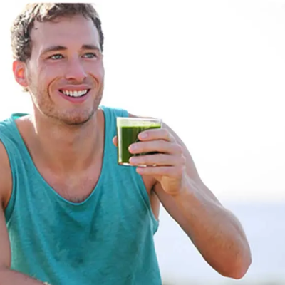 9 Essential Nutrients You Need to Combat Thinning Brittle Hair - a man in a teal tank top drinking green juice outside after working out.