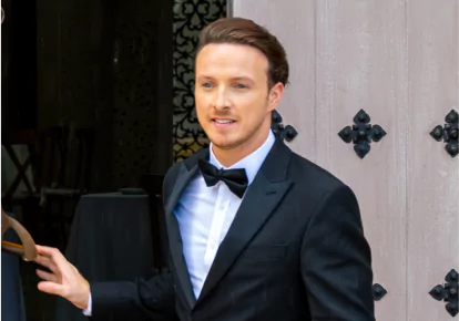 A man wearing a black suit, white button-down shirt, and black bowtie